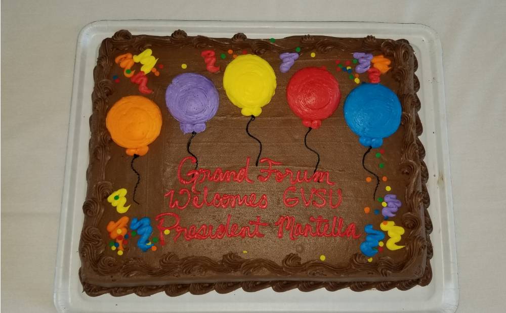 A chocolate cake with frosting balloons and a message that reads "Grand Forum Welcomes GVSU President Mantella"